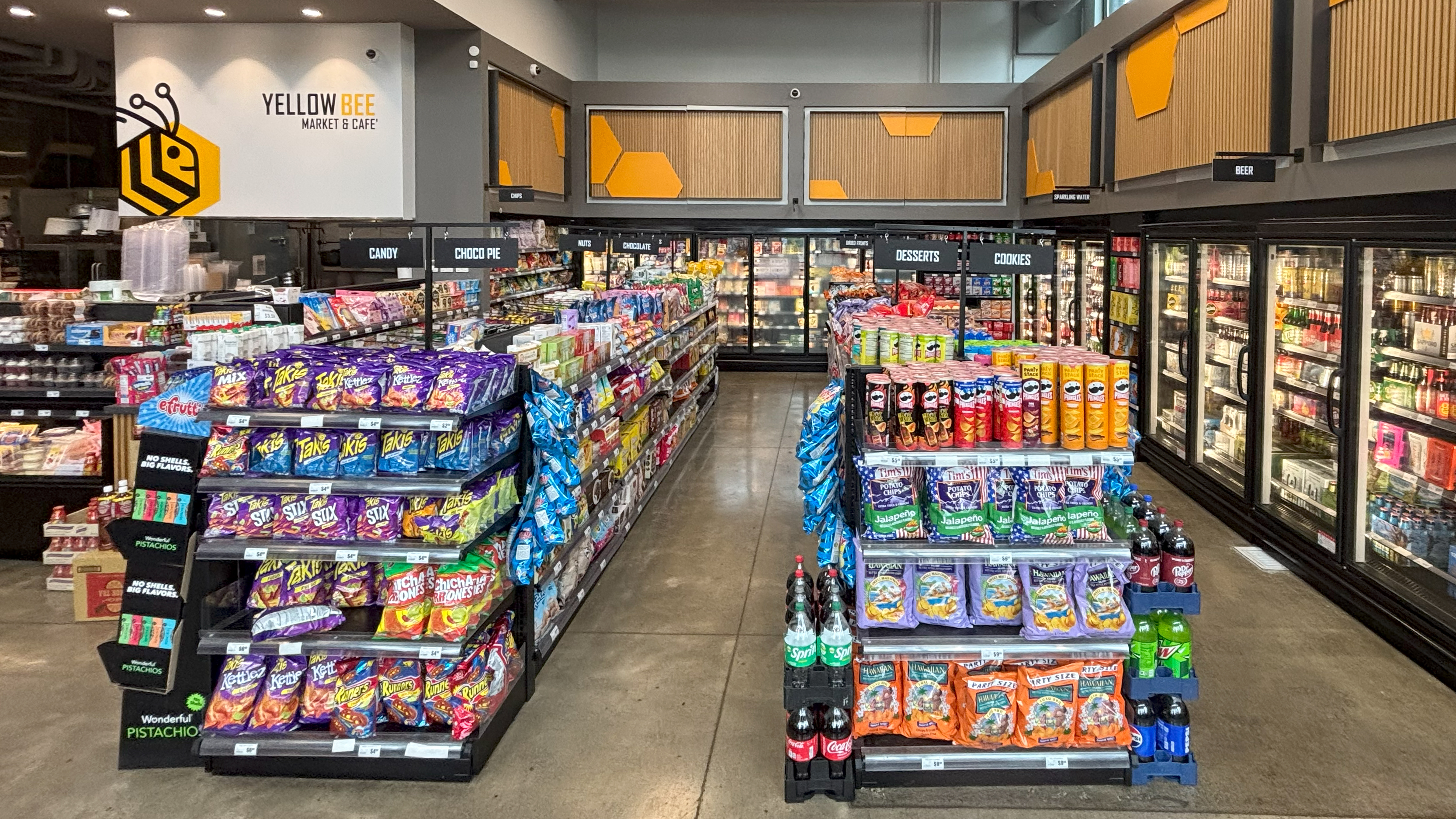 Aisle view at Yellow Bee Market & Cafe in Seattle’s Yesler neighborhood, featuring bold black aisle signs for candy, desserts, and cookies above neatly stocked shelves.